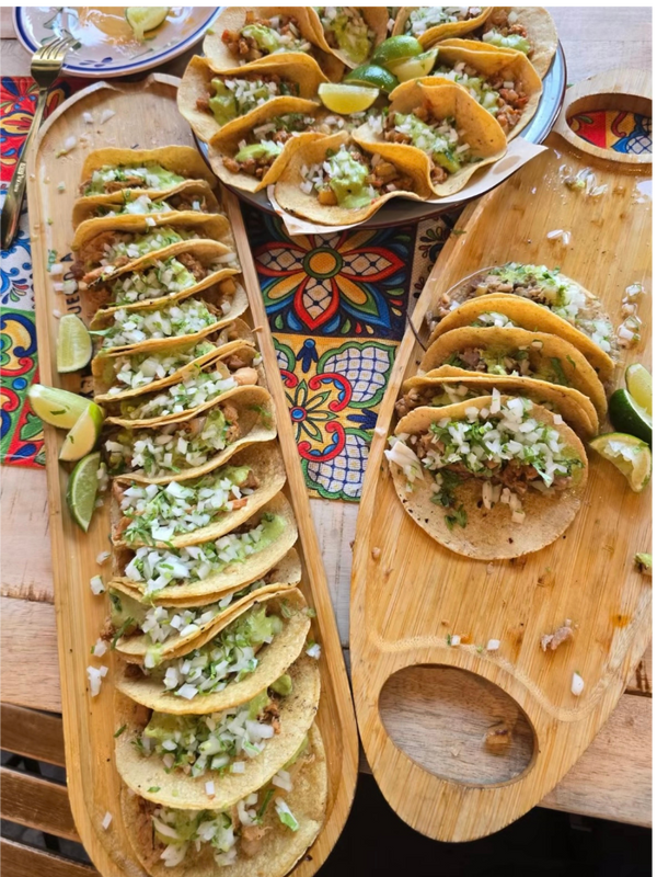 Wooden platter with tacos garnished with lime wedges on a colorful tablecloth.