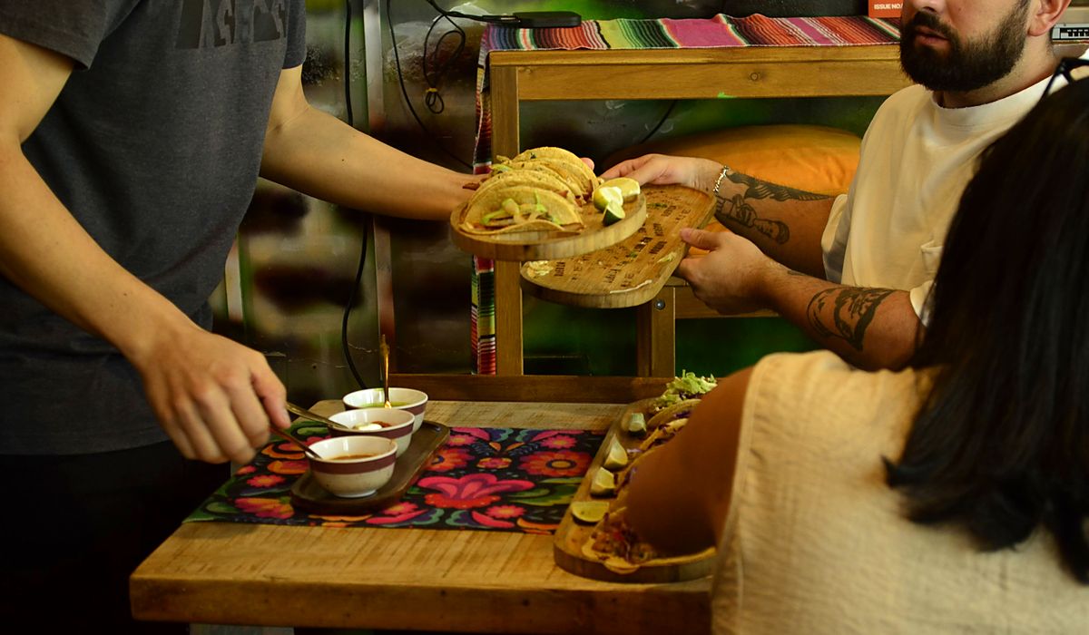A board of Tuesday tacos with lime passed across a Querida table, salsas in small bowls beside it