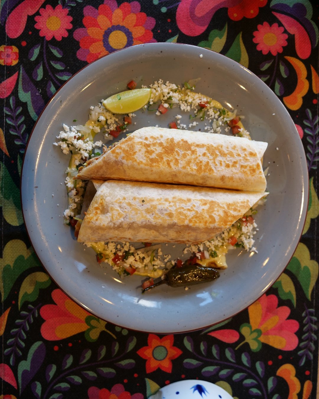 A hand-rolled Querida burrito, griddle-pressed and sliced, plated with lime, pico de gallo, cotija and a roasted jalapeño — the burrito you'll learn to roll at the masterclass.
