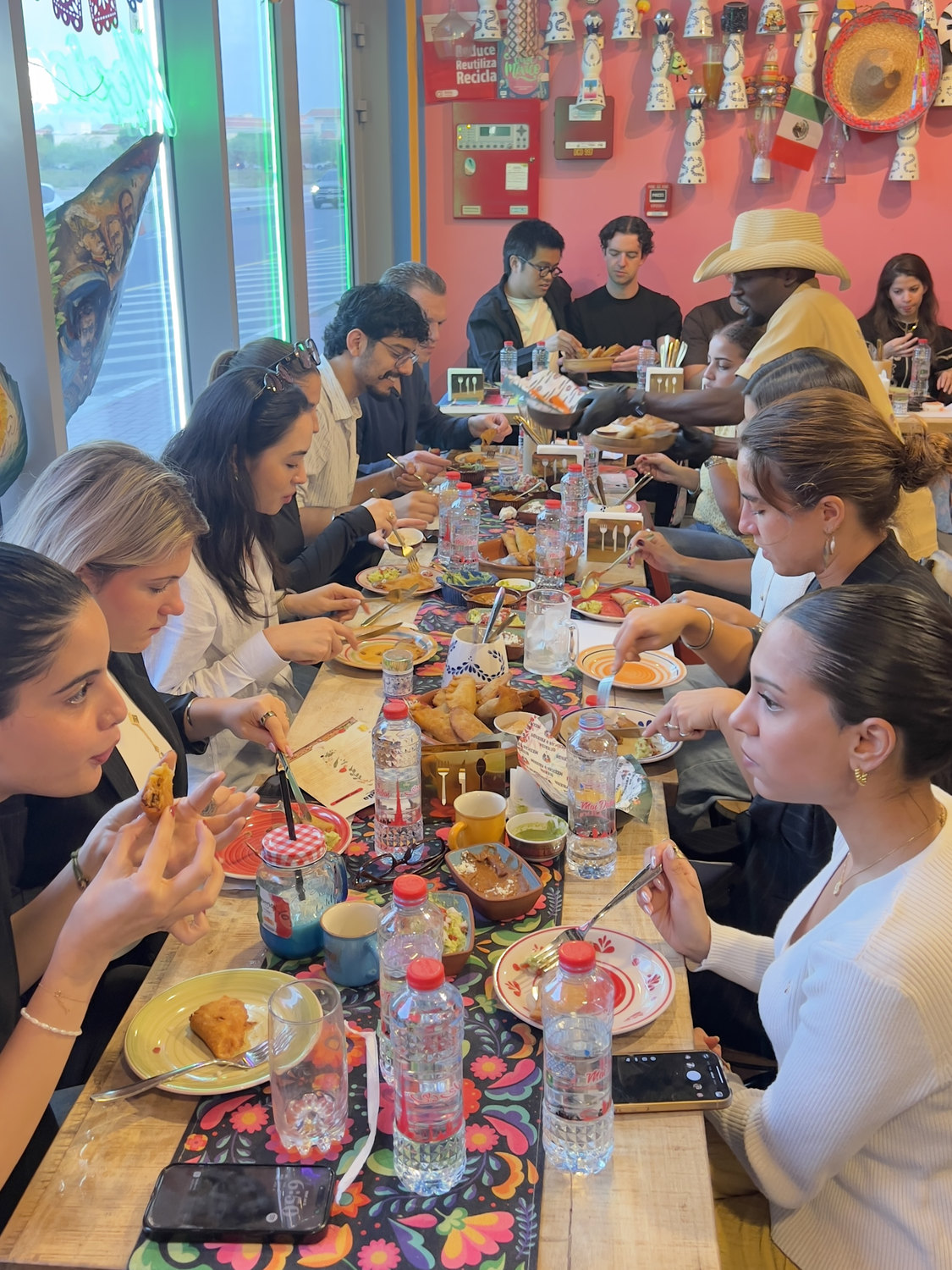 The long table at Querida mid-class — guests eating what they just made, under the pink mural wall