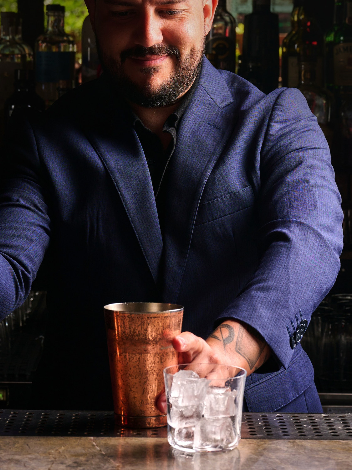 Mariano Conde building a drink behind the bar, setting a copper tin down beside a glass of ice