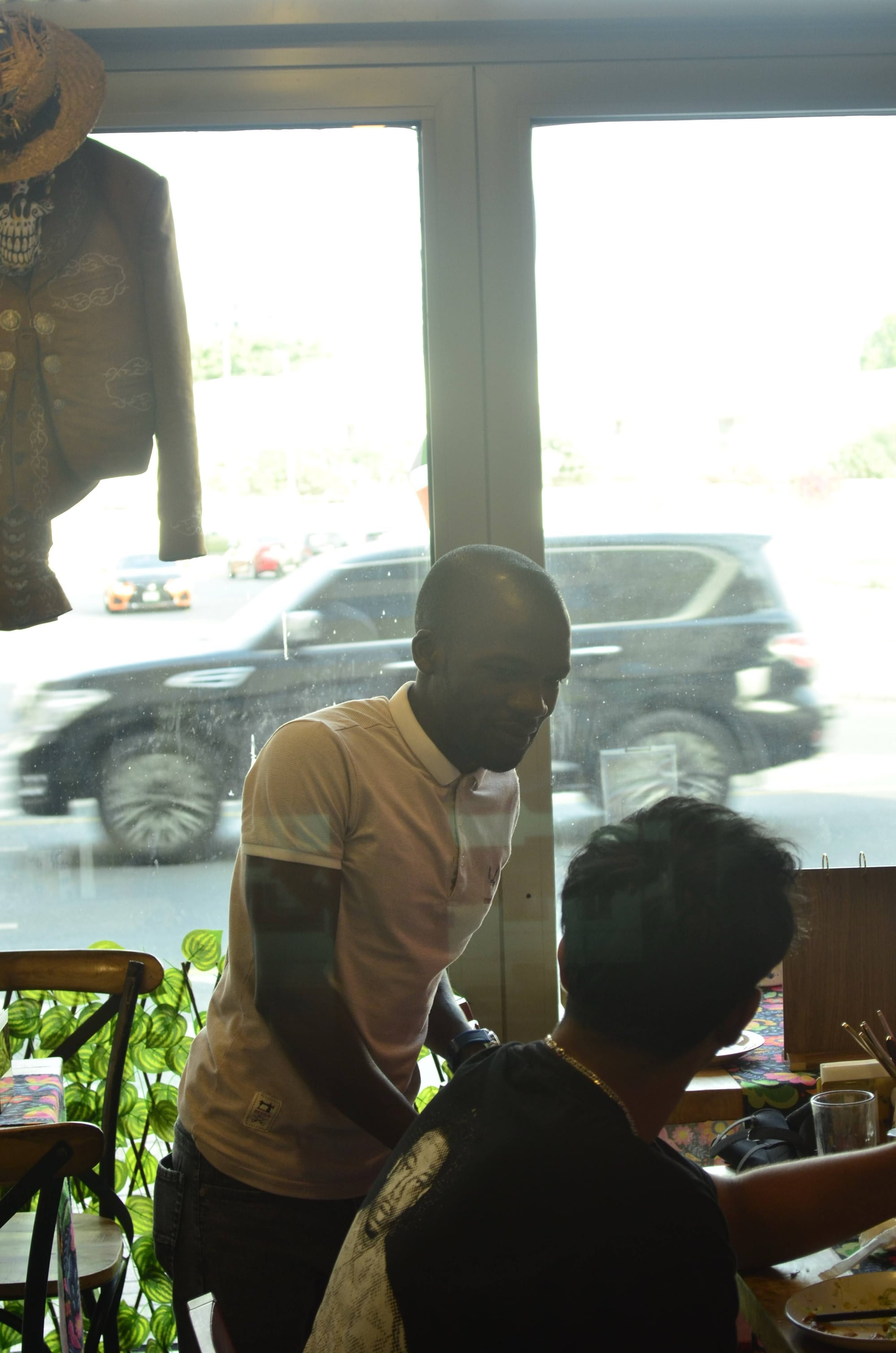 Querida server placing the first plate of the night on a corner two-top, mid-action close-up