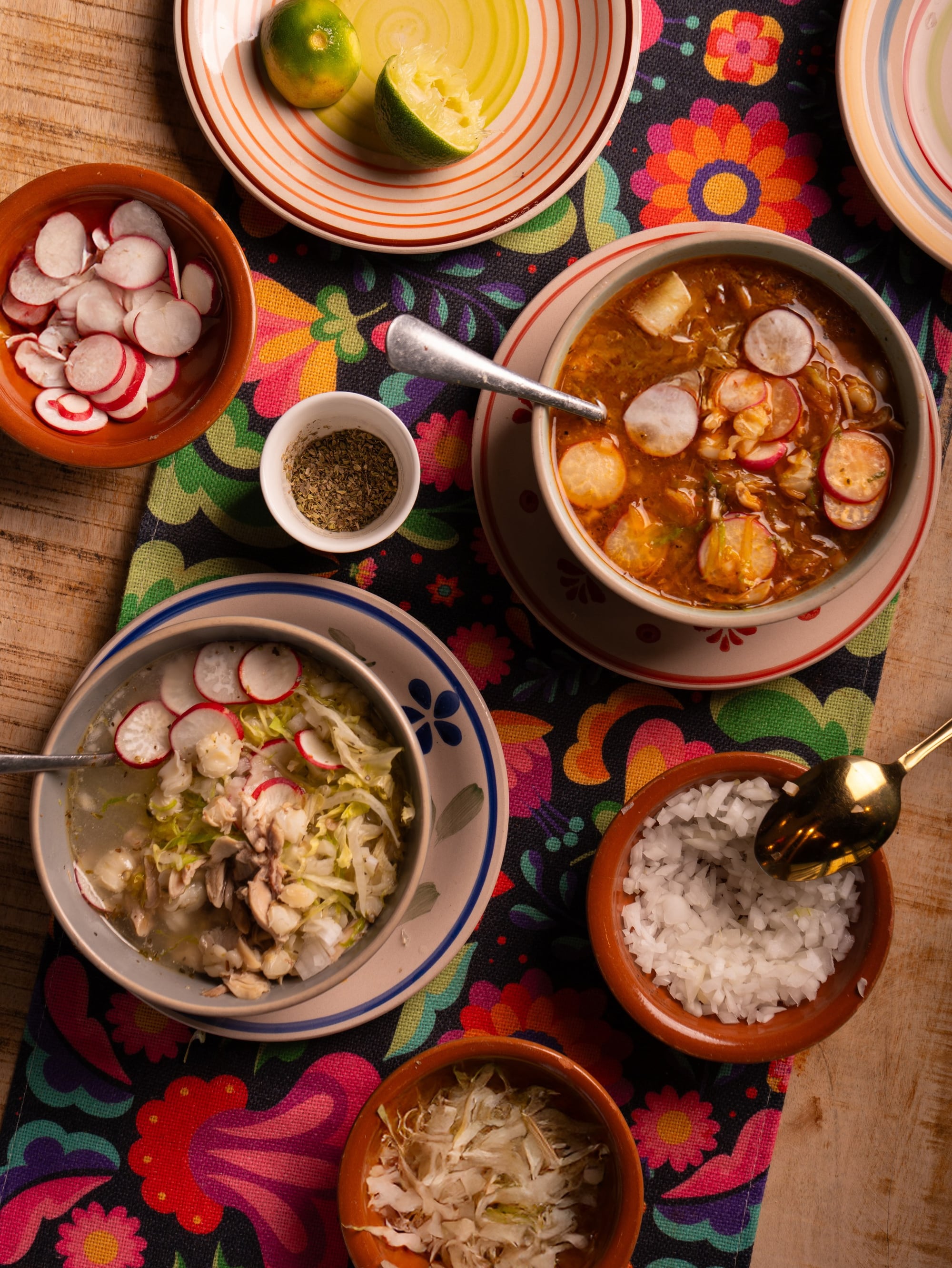 Pozole rojo and blanco with the full plate of fixings — radish, cabbage, raw onion, lime, tostadas