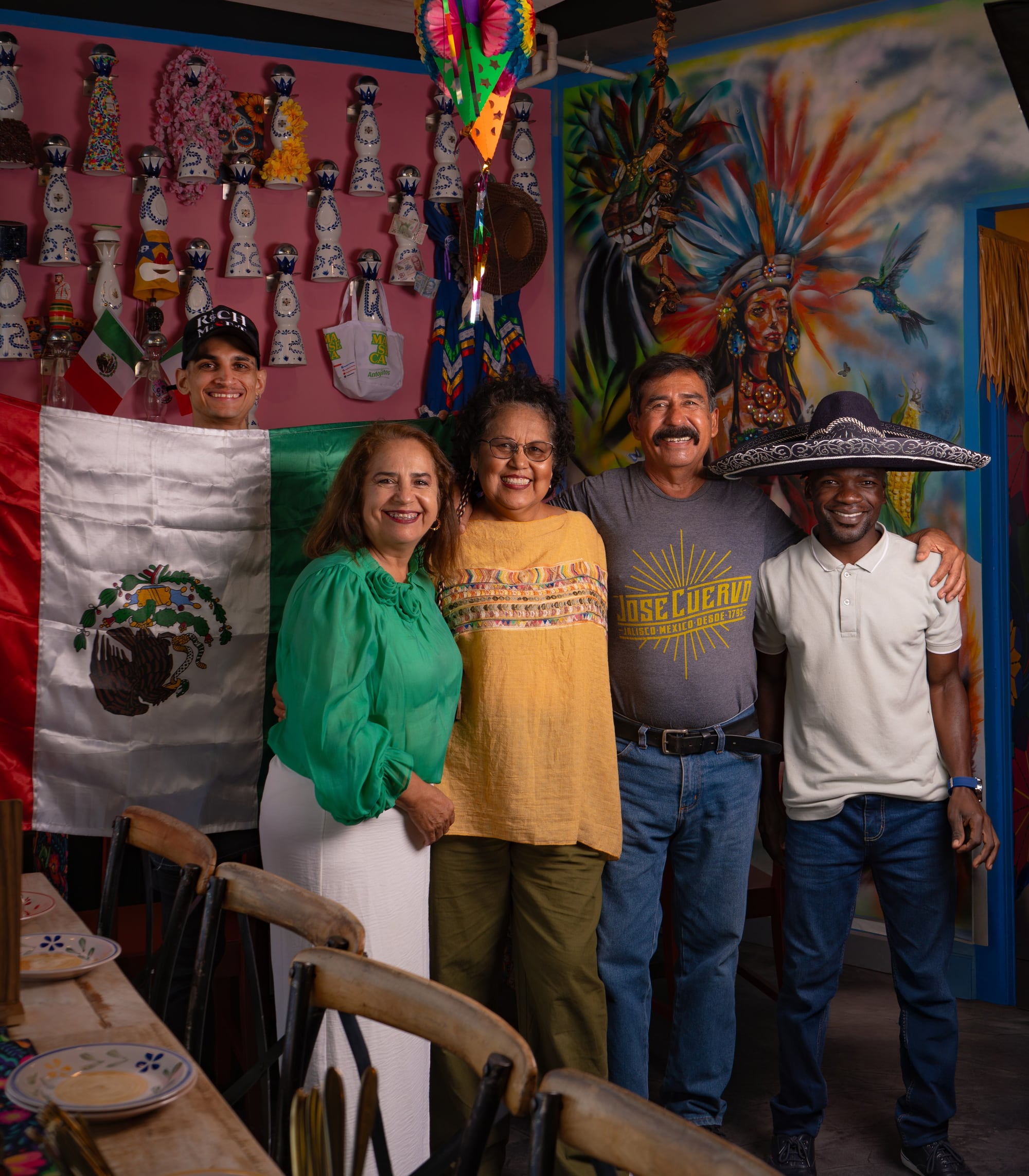 The Querida team in front of the Mexican flag and the Catrina mural — Sagar, Mama Lalis, the brigade and the front-of-house