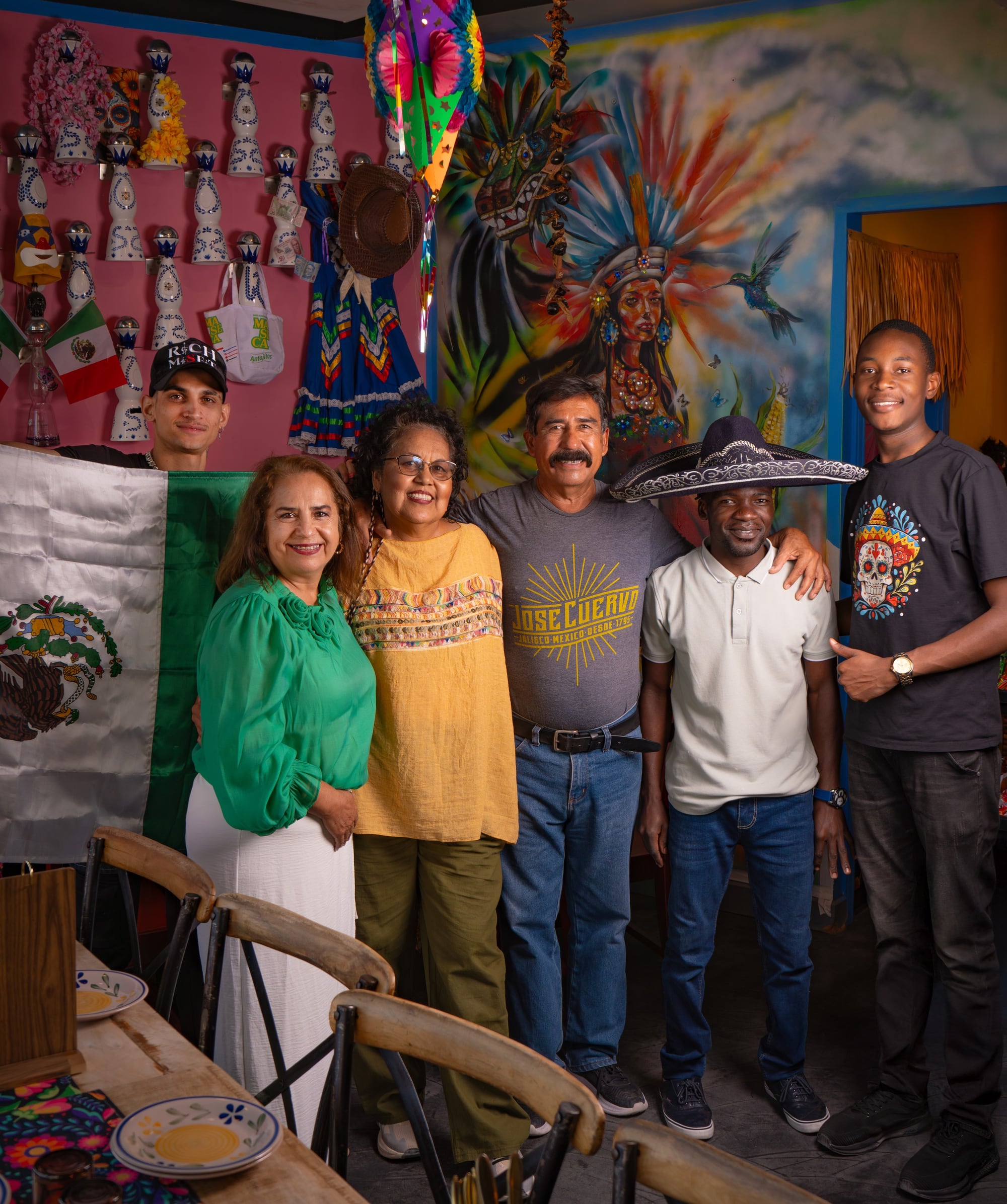 The Querida team in front of the Mexican flag, the Catrina mural, sombrero in hand