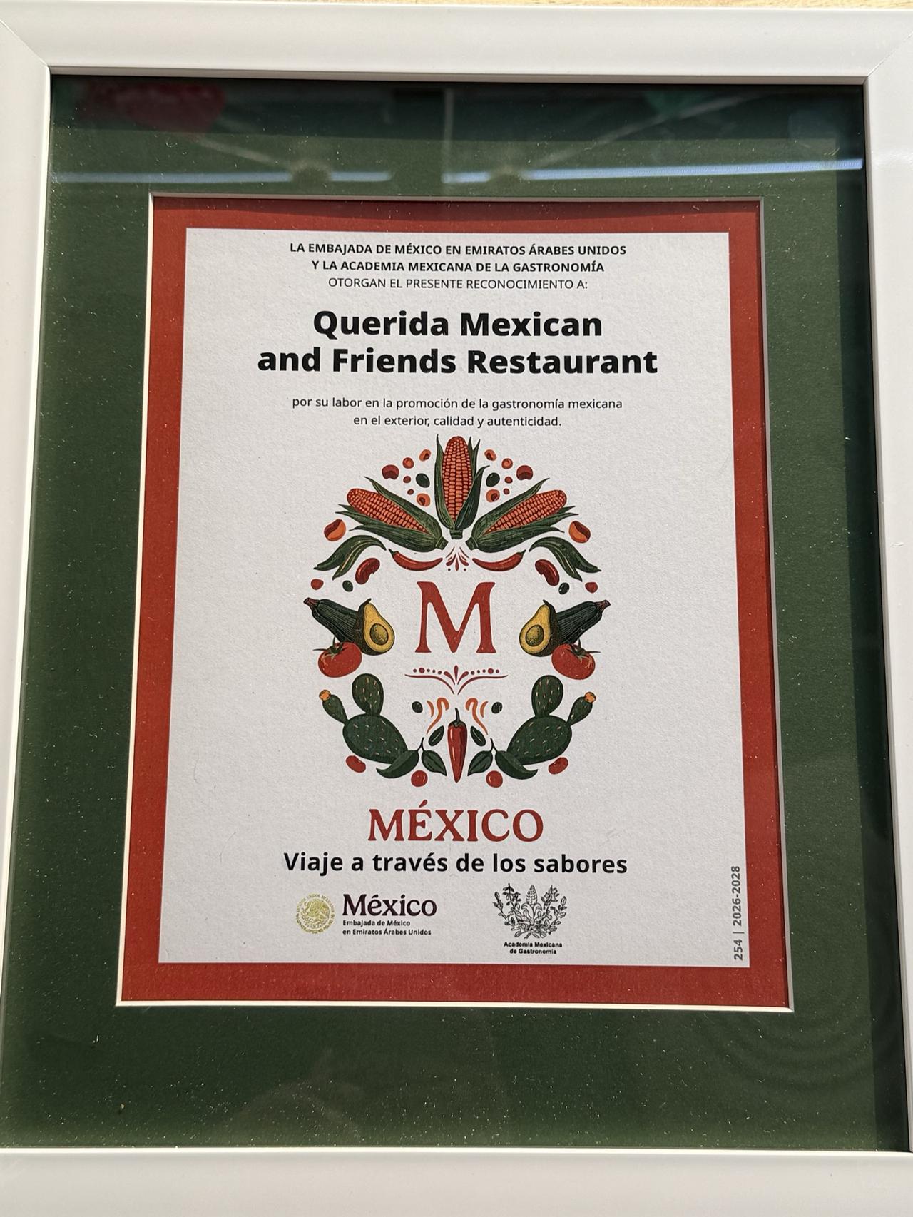 The framed certificate: Reconocimiento No. 254 from the Embassy of Mexico in the UAE and the Academia Mexicana de la Gastronomía to Querida Mexican and Friends Restaurant, 2026–2028, in a white frame with a green mount